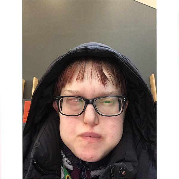 Jenny is wearing glasses whilst wearing a blue hoodie looking into the camera