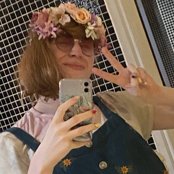Rae is wearing glasses with flower crown in hair taking a selfie