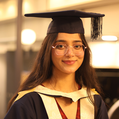 Ashween with glasses smiling to camera wearing the BCU graduation gown and cap