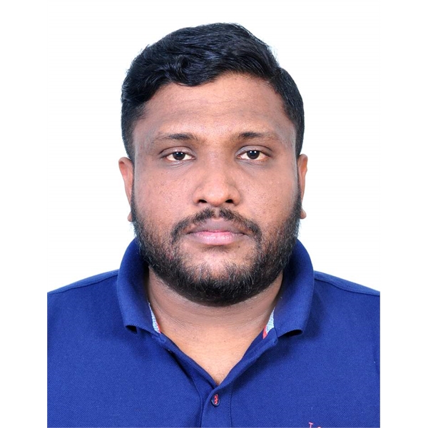 Sebin has black hair and black beard and is sitting down wearing a blue t-shirt