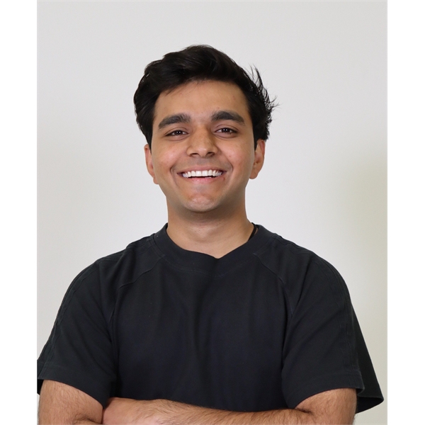 Wahid has black hair and clean shaven and is posing with his arms crossed with a black t-shirt on